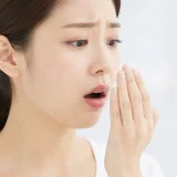 자신의 입 냄새를 확인하며 걱정하는 여성의 모습
