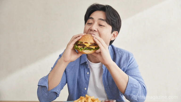 한 남성이 두 손으로 빅아치 버거를 들고 맛있게 먹고 있다.